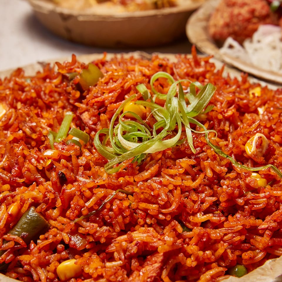 Close-up of vibrant orange Nepalese fried rice with green onions, corn, and peppers in a bowl.