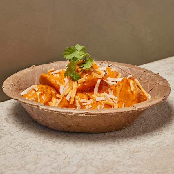 Orange-sauced dumplings topped with shredded cheese and cilantro in a brown bowl.