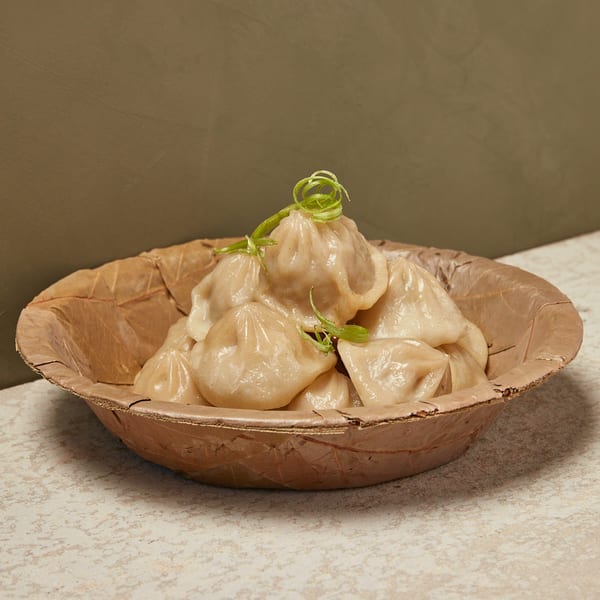 Steamed dumplings, garnished with green onion curls, in a rustic, leaf-shaped bowl.