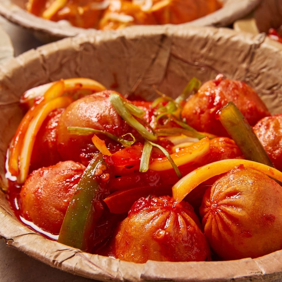 Close-up of Momo Souls' Nepalese momos in a red sauce with peppers and onions, served in a leaf bowl.
