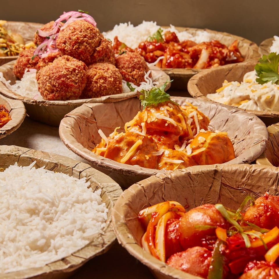 Assortment of Nepalese dishes in leaf bowls, including fried momos, rice, and saucy chicken.