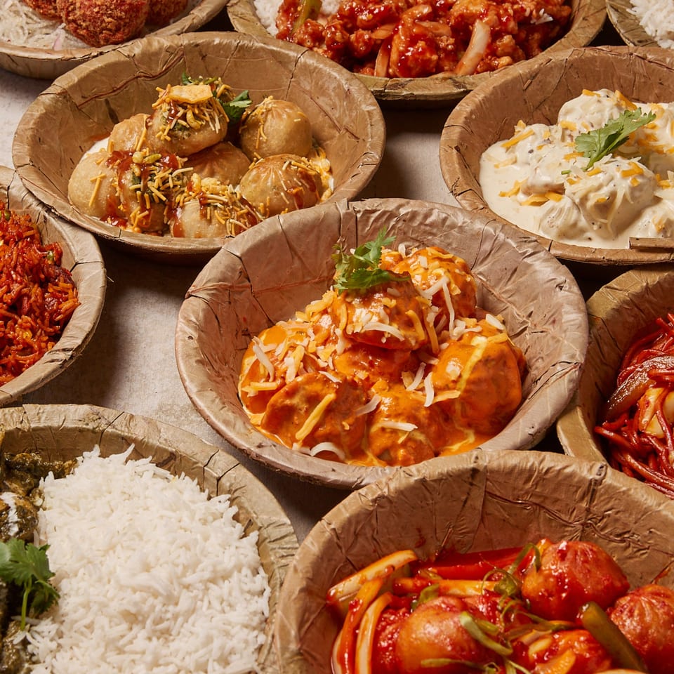 Assortment of Nepalese dishes, including momos with various sauces, rice, and noodles, in eco-friendly bowls.