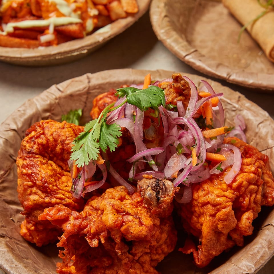 Crispy fried chicken topped with red onions, carrots, and cilantro in a brown bowl.