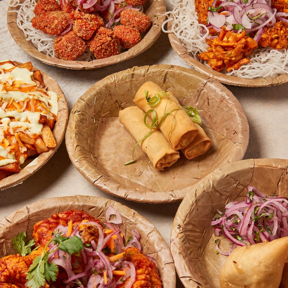 A variety of Nepalese dishes, including spring rolls, fried chicken, and samosas, in eco-friendly bowls.