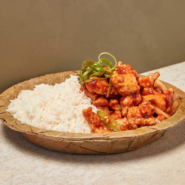 Sweet and sour chicken with white rice and green onions in a natural fiber bowl.