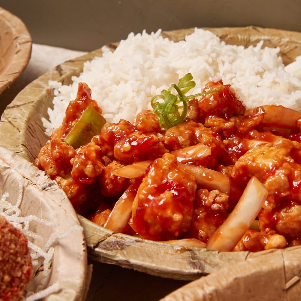 Sweet and sour chicken with white rice and green onions in a natural bowl.