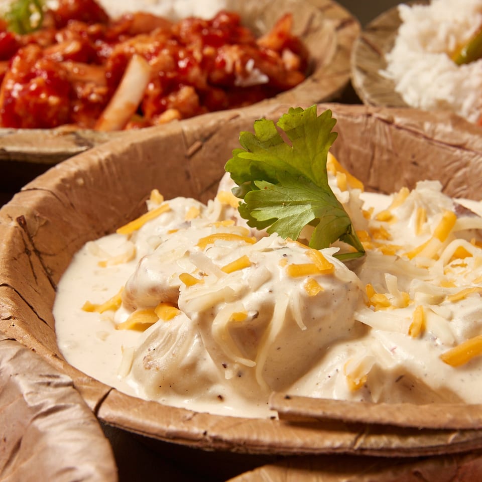 Creamy Nepalese momo dumplings topped with shredded cheese and cilantro, served in a leaf bowl.