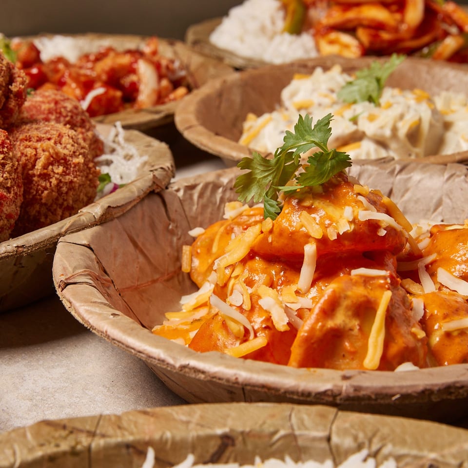 Close-up of Momo Souls' Nepalese momos with orange sauce, cheese, and cilantro in a leaf bowl.